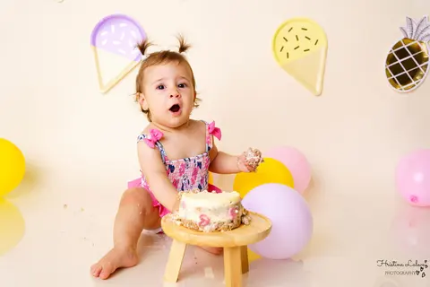 Момиченце на smash cake фотосесия възкликва учудено с ръчичка, цялата в торта