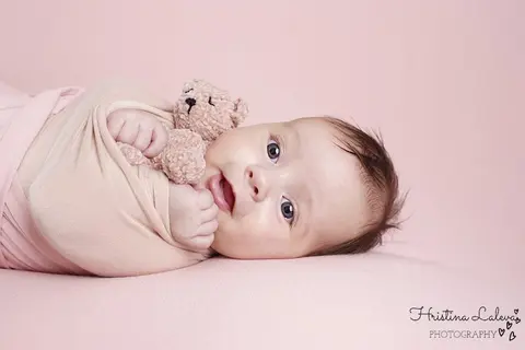 Будно бебе със сини очи, повито в розово, гушка меко мече